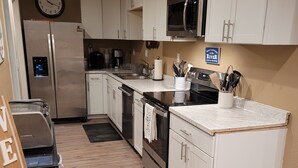 A modern kitchen with white cabinets, a stainless steel refrigerator, a microwave, and a sink.