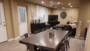 A spacious dining area with a long table and chairs, a kitchen in the background, and a 'WELCOME' sign.