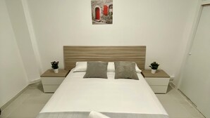 Habitación de hotel ordenada con una cama grande, dos mesitas de noche y una pequeña maceta en cada lado.