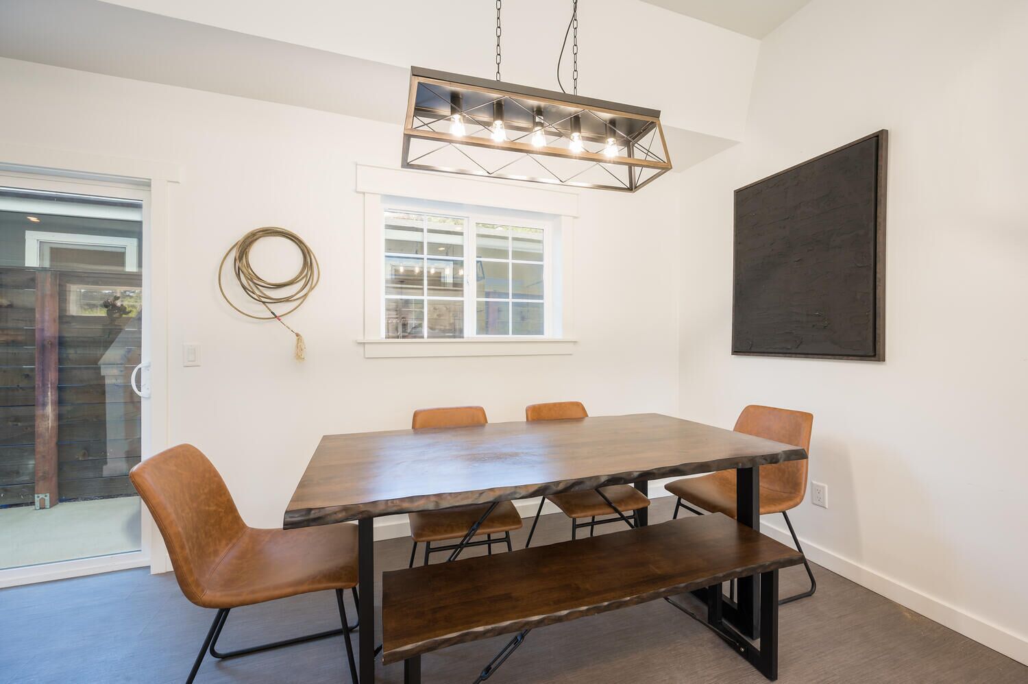 A dining area with a rectangular table, six chairs, a pendant light, a window, and a large abstract painting on the wall.