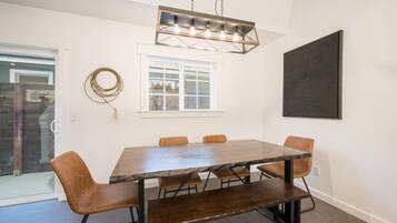 A dining area with a rectangular table, six chairs, a pendant light, a window, and a large abstract painting on the wall.