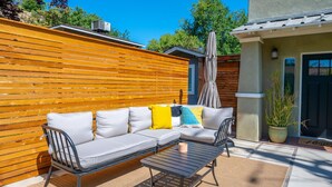 A wooden fence, a gray sofa with cushions, a metal table, and a potted plant. - Swanky Downtown Cowboy (Paso Robles)