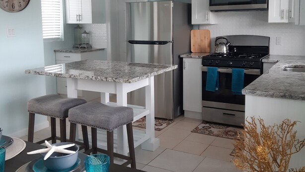 A modern kitchen with white cabinets, stainless steel appliances, and a dining area with a table set for two. - La Nueva Beach home two minute walk to beach & 1 minute walk to the golf course (Abaco)