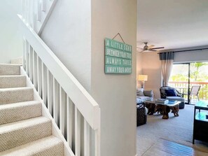 A staircase with a sign on the wall, a living room with a sofa, a coffee table, and a view of the outdoors.
