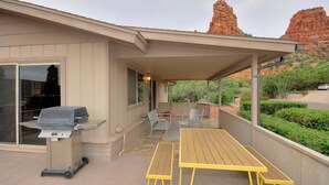 A covered patio with a grill, outdoor seating, and a view of red rock formations.
