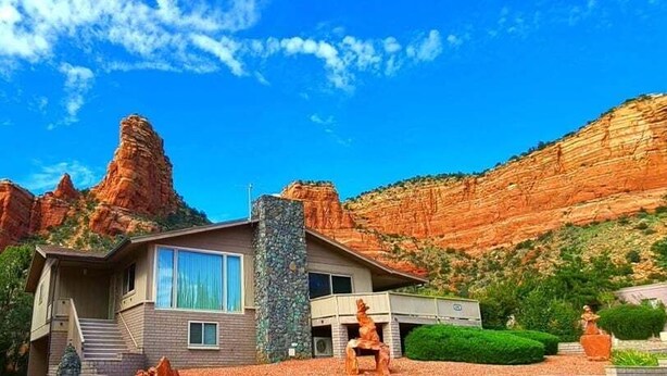 A modern house with a stone facade, large windows, and a view of red rock formations.