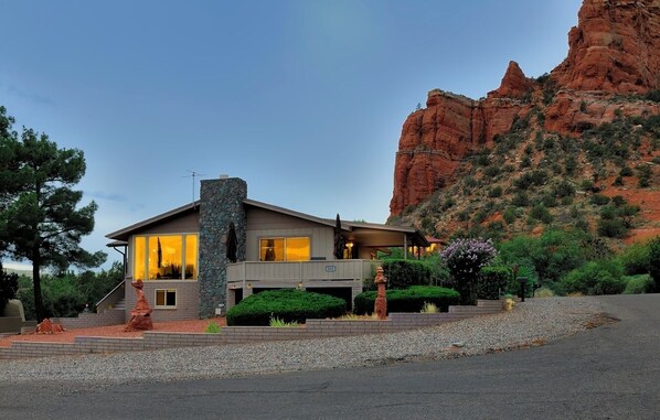 A modern house with a stone chimney, large windows, and a view of a red rock formation.