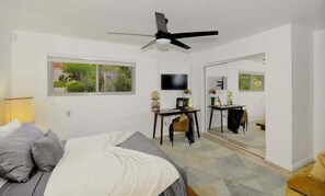Ein Schlafzimmer mit Bett, Schreibtisch, Stuhl, Fernseher und Deckenventilator.