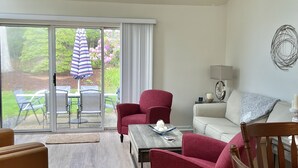 A spacious living room with a large sliding glass door leading to a patio area. There is a red armchair, a wooden coffee table, and a white sofa. - Sunlit townhome at Ocean Edge Resort in Brewster- central A/C, pool privilege's (Brewster)