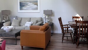 A modern living room with a high ceiling, a large painting, a sofa, a coffee table, and a dining area with chairs. - Sunlit townhome at Ocean Edge Resort in Brewster- central A/C, pool privilege's (Brewster)