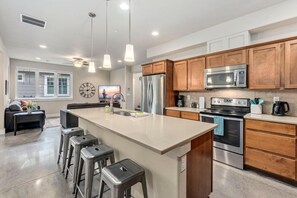 A modern kitchen with a large island, stainless steel appliances, wooden cabinets, and bar stools. - Exceptional Solar Powered Home near Old Town! (Fort Collins)