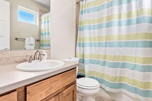 A bathroom with a striped shower curtain, a sink, and a toilet. - Contemporary Solar Powered Studio near Old Town! (Fort Collins)