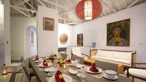 Un coin repas avec une longue table dressée pour le repas, entouré de chaises en osier et d’un canapé.