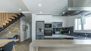 Une cuisine moderne dotée d’un îlot central, d’appareils électroménagers intégrés et d’un escalier avec des poutres apparentes.