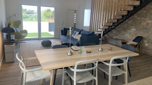 Un salon moderne avec une table à manger en bois, des chaises blanches, un canapé bleu et un escalier avec des rampes en bois.