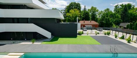 Un edificio moderno con zona de piscina, que incluye una terraza de madera y una piscina azul cristalina.