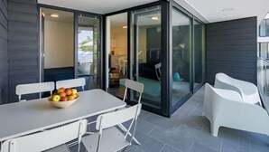 A modern outdoor dining area with a table and chairs, a bowl of fruit, and a view into the adjacent kitchen and living space. - Fenyves by Interhome (Balatonszemes)