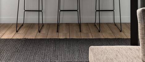 A modern room with a large window, three black metal stools, a white plant, and a grey rug.