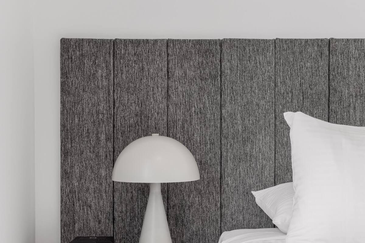 A neatly made bed with white bedding, a white lamp on a bedside table, and a modern alarm clock.