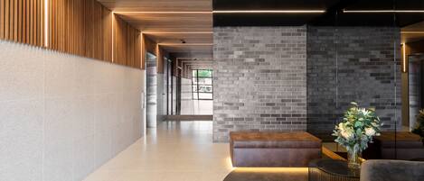 Eine moderne Lobby mit einer Holzdielen-Decke, einer Ziegelwand und einer Sitzecke mit einem Blumenstrauß.