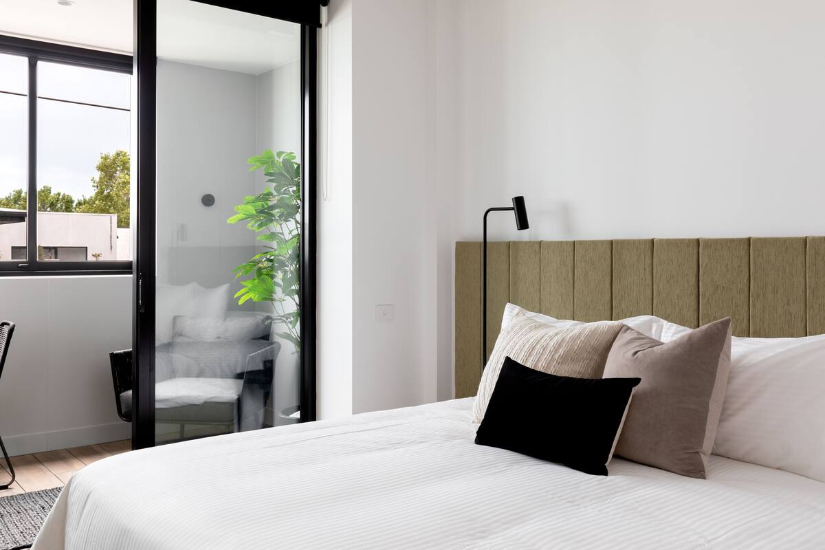 A modern bedroom with a large bed, a bedside table, a chair, and a view of the outdoors.
