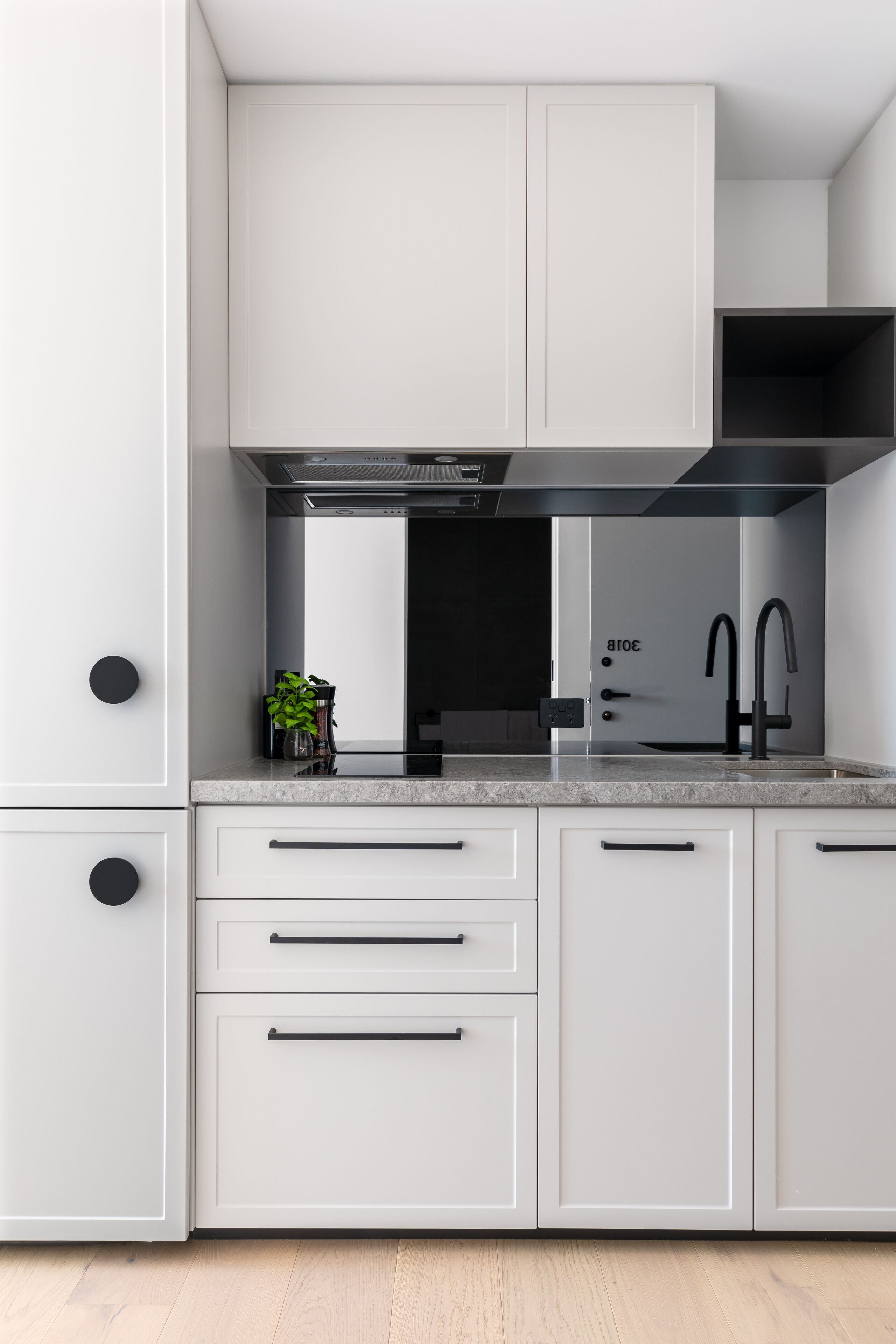 A modern kitchen with white cabinetry, black handles, and a stainless steel range hood.