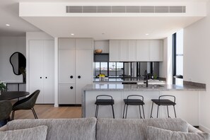 A modern kitchen with a central island, bar stools, and a dining area with a round table and chairs. - Caroline Serviced Apartments Richmond (Richmond)