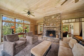 A cozy living room with a stone fireplace, comfortable seating, and large windows.