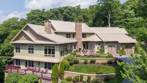 A large, two-story house with a stone chimney, a covered porch with chairs, and a well-maintained lawn.