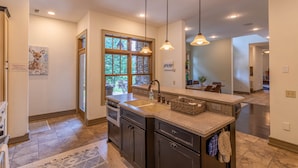 A modern kitchen with dark cabinets, a granite countertop, a large window, and pendant lighting.