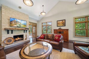 A spacious living room with a fireplace, leather sofa, and large windows.