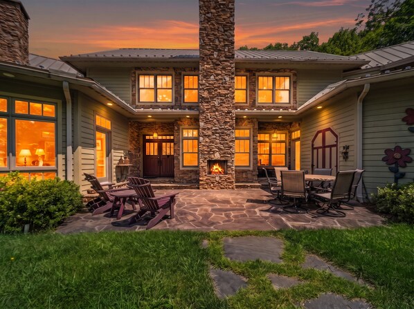 A two-story house with a stone fireplace, outdoor seating, and a well-maintained lawn.
