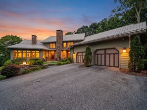 A two-story house with a stone chimney, a gravel driveway, and a garage with a dark door.