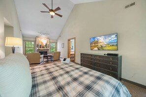 A bedroom with a bed, a desk, a chair, a dresser, a television, and a ceiling fan.