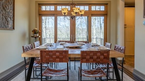 A dining area with a large wooden table, leather chairs, and a chandelier.
