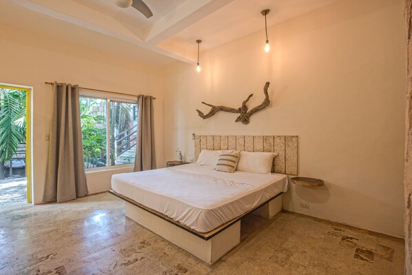 A bedroom with a large bed, a wooden headboard, a bedside table, and a window with curtains. - Master Room on 5th (Playa del Carmen)