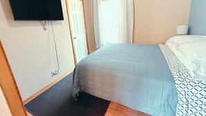 Makuuhuone, jossa on sänky, seinälle asennettu taulutelevisio, ovi ja ikkuna, jossa on verhot.