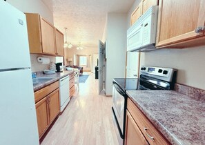 A kitchen with wooden cabinets, a refrigerator, a stove, and a microwave. - Foosball|Cottage by McKennan|Fenced inYard (Sioux Falls)