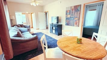 Una sala de estar con un sofá, una mesa de comedor con sillas, un televisor sobre un mueble bajo y un cuadro en la pared.