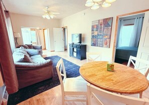 A living room with a sofa, a dining table with chairs, a TV on a stand, and a painting on the wall. - Foosball|Cottage by McKennan|Fenced inYard (Sioux Falls)