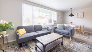 A modern living room with a grey sectional sofa, a wooden coffee table, and a large window with blinds.