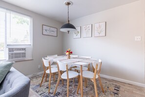 A dining area with a round table, white chairs, and a hanging pendant light.