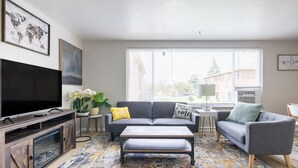 A modern living room with a flat-screen TV, grey sofas, a coffee table, and a patterned rug.