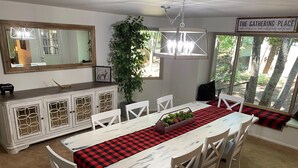 Un espace repas avec une longue table, des chaises blanches, un chemin de table à carreaux rouges et noirs, et un luminaire suspendu.