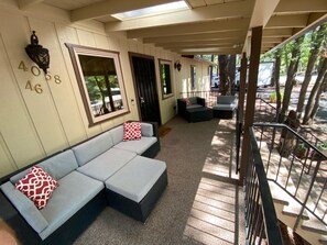 A covered outdoor seating area with a light blue sofa and red patterned pillows, a large window, and a view of the street. - Beautiful Hillside home in exclusive Pinetop Country Club, perfect for families (PineTop)