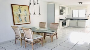 A modern kitchen with white cabinets, a black countertop, and a glass dining table with wicker chairs.