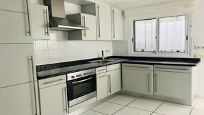 A kitchen with white cabinets, a Bosch oven, a black countertop, and a window with white curtains.