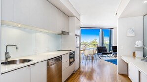 A modern kitchen with a built-in dishwasher, a stainless steel sink, and a large window overlooking a cityscape. - PEP 4305/6 - 2 Bedroom Apartment (Kingscliff)