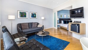 A modern living room with a grey sofa, black leather chairs, a round coffee table, and a flat-screen TV mounted on the wall. - PEP 4305/6 - 2 Bedroom Apartment (Kingscliff)