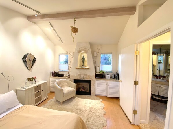 A bedroom with a bed, a chair, a fireplace, a vanity, and a mirror. - Serene Montclair Getaway (Oakland)